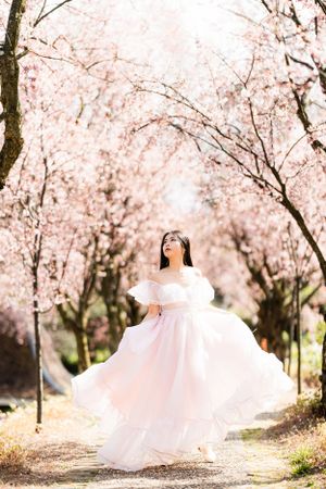 A graceful figure twirls in a white dress under an archway of delicate pink cherry blossoms.