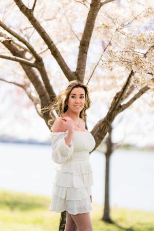 White ruffle dress and flowing hair captured in soft sunlight under blooming spring trees.