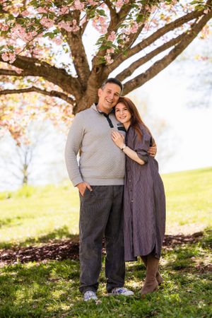 A couple in cozy sweaters embrace under a blooming cherry blossom tree on a sunny spring day.