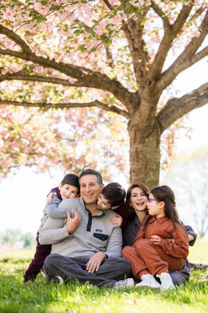 A family sits together on grass under a blooming cherry blossom tree in spring.