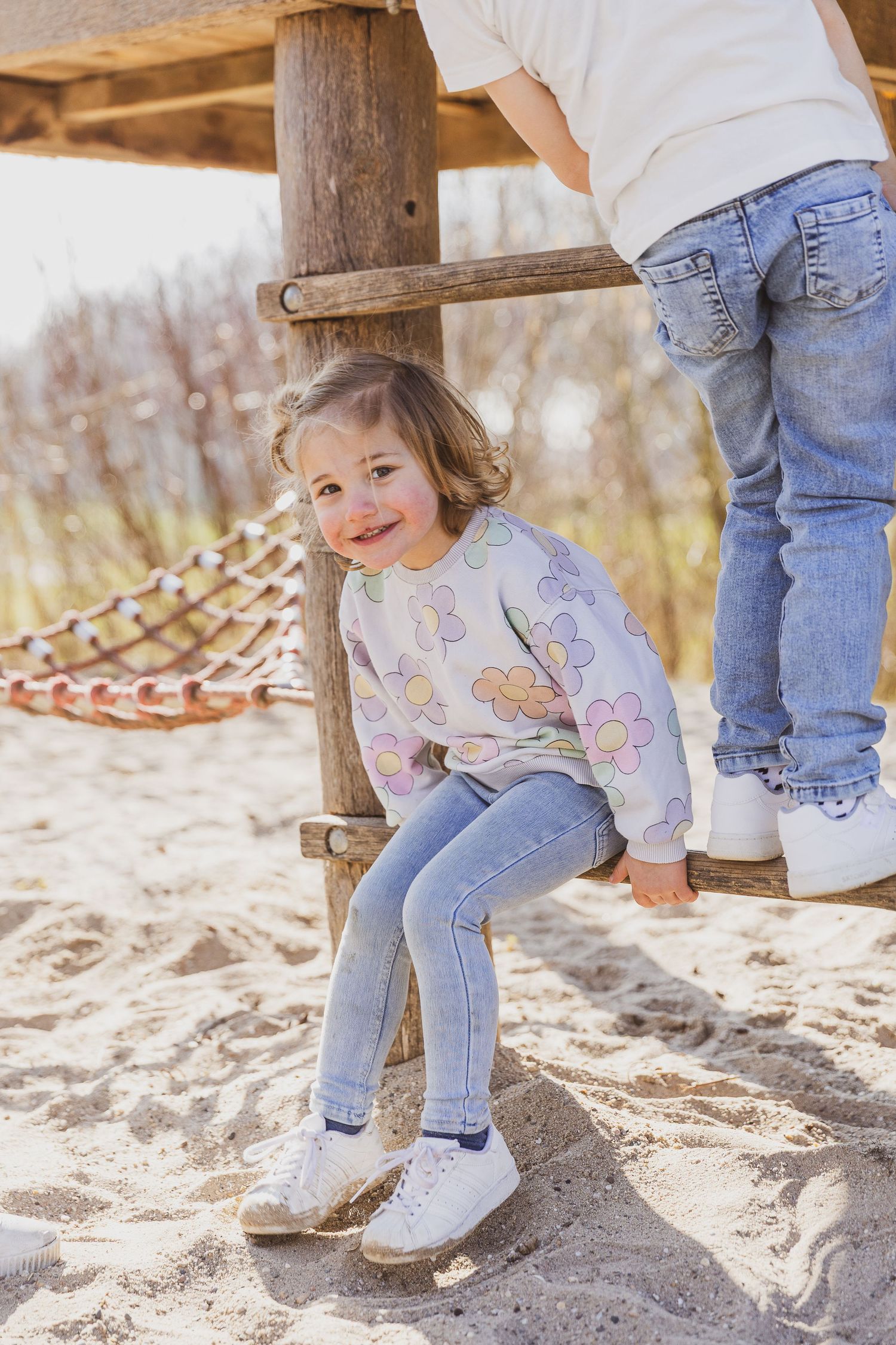 Child sitting on wooden playground structure wearing floral sweater and jeans. Kinderen in ongedwongen sfeer foto.