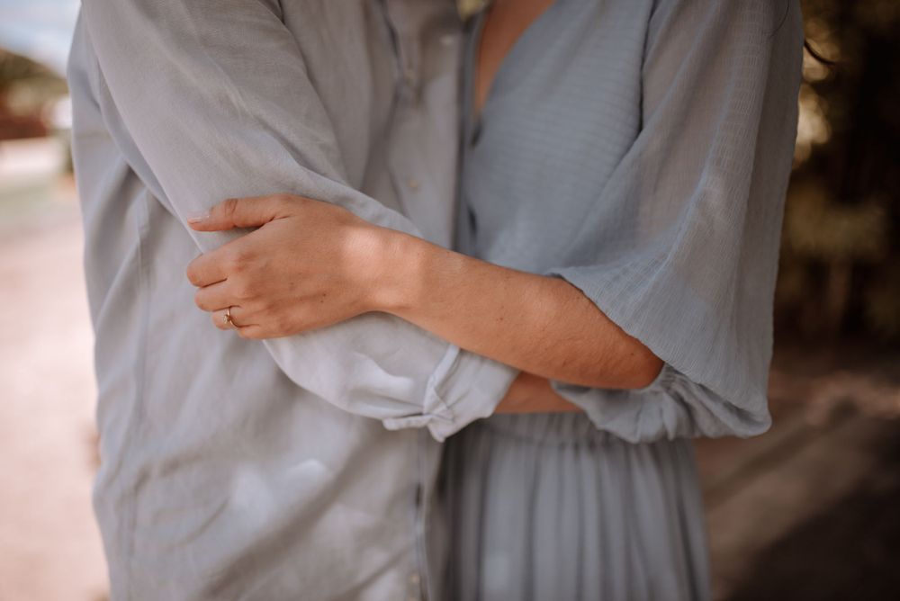 Close-up of crossed arms in a light blue flowy dress against a soft background.