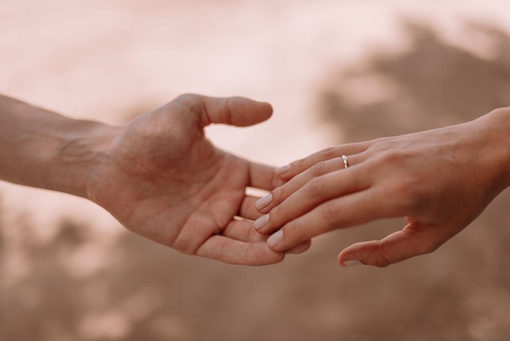 Close up of hands reaching towards each other with a ring in soft lighting.