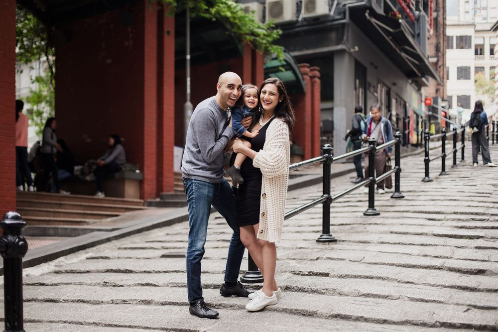People stand together laughing and smiling on historic stone steps in an urban setting with black railings and brick walls.