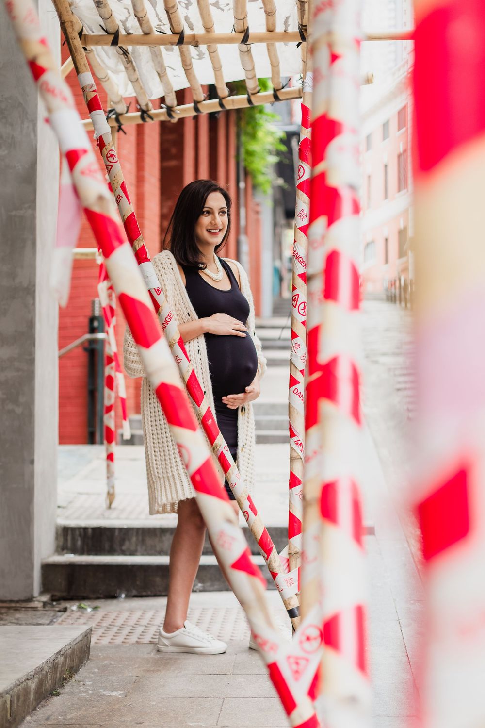 Maternity photo shoot along a red and white striped decorated urban corridor with a woman in a black outfit.