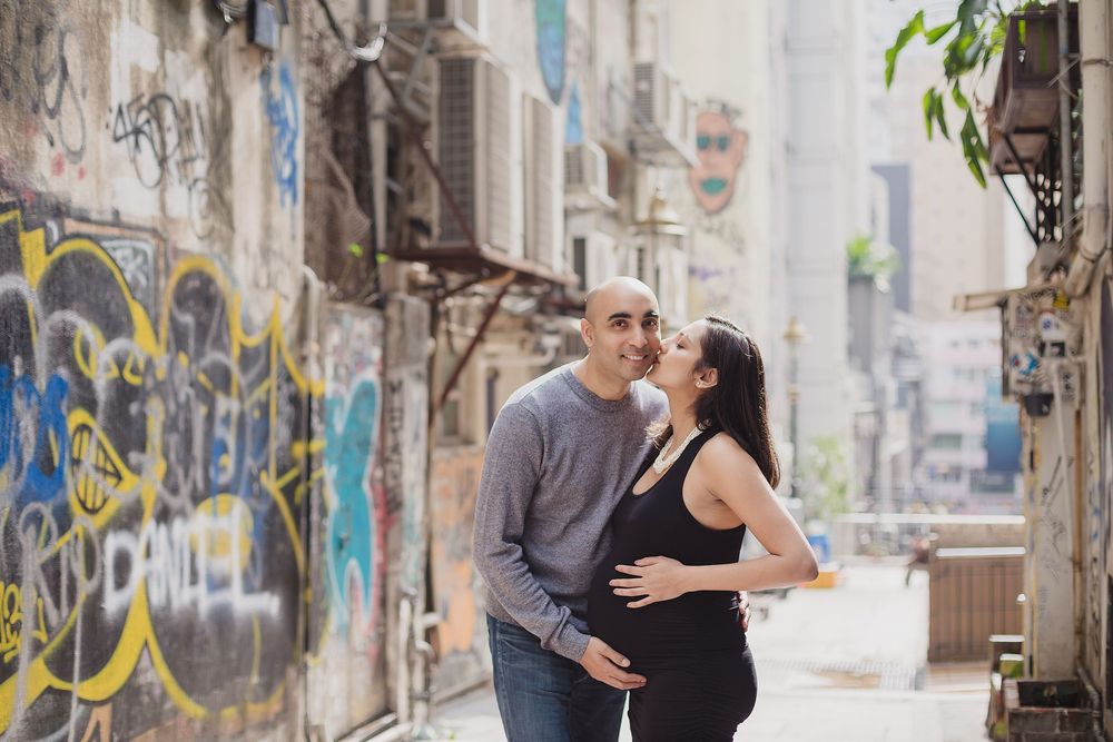 A couple poses intimately together on a graffiti-covered urban street wall for engagement style photos.