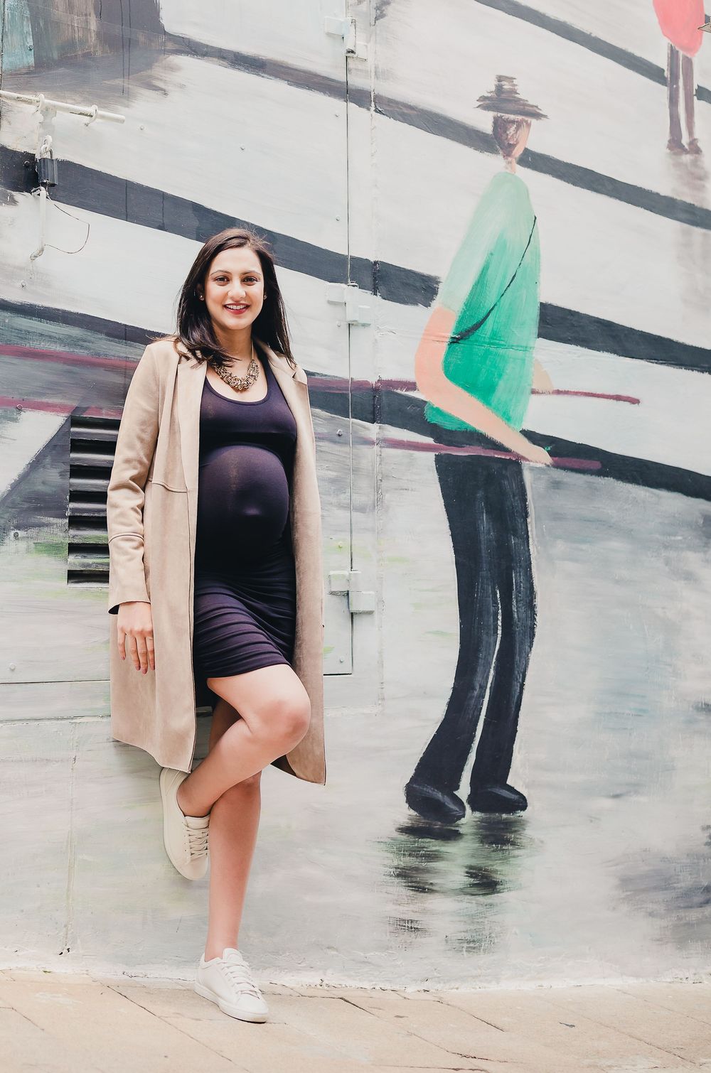 A person wearing a black swimsuit and beige blazer poses on a wet concrete surface near tall walls.
