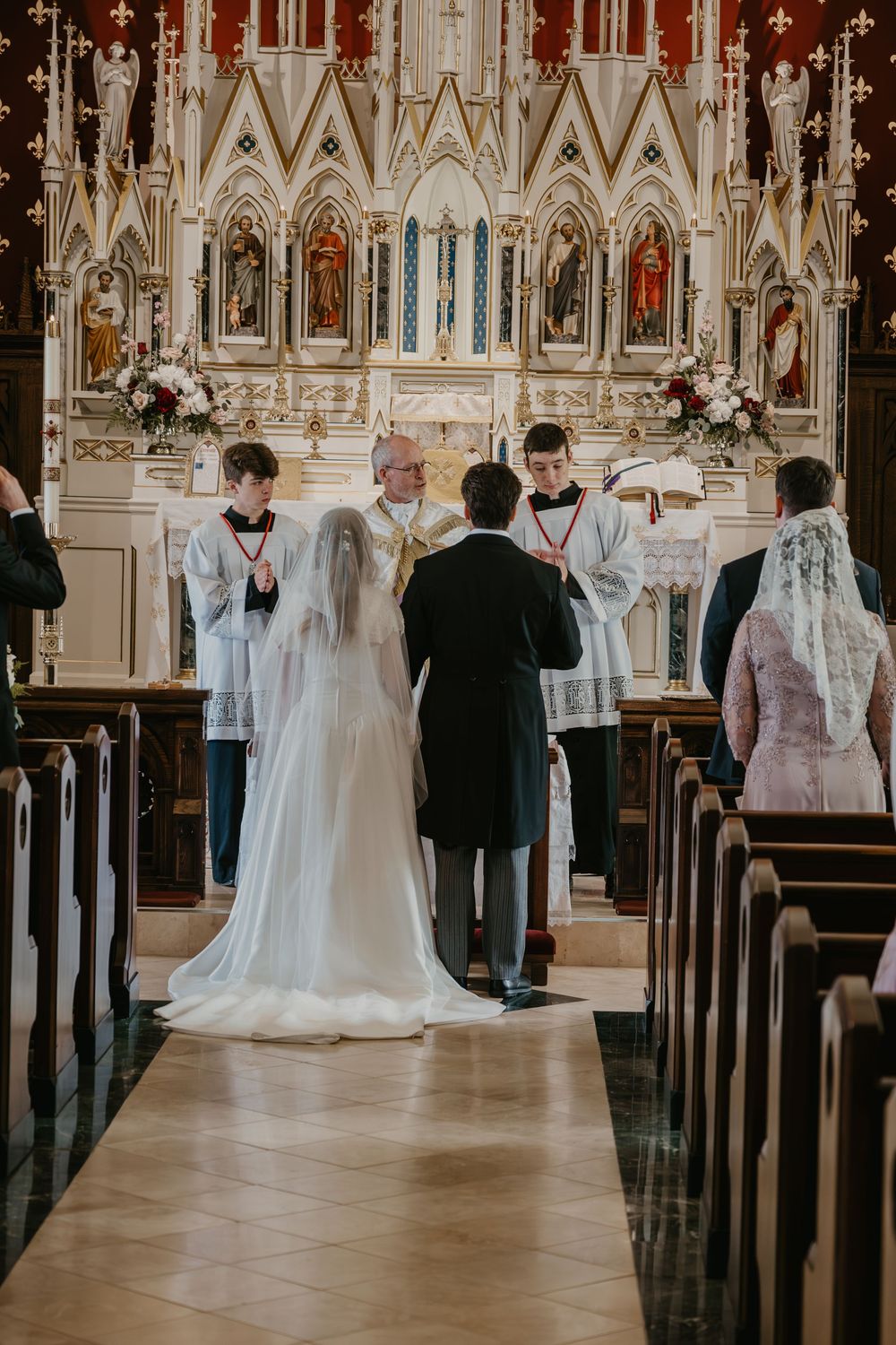 Bride and groom standing at grand Gothic Catholic church altar during traditional wedding ceremony.