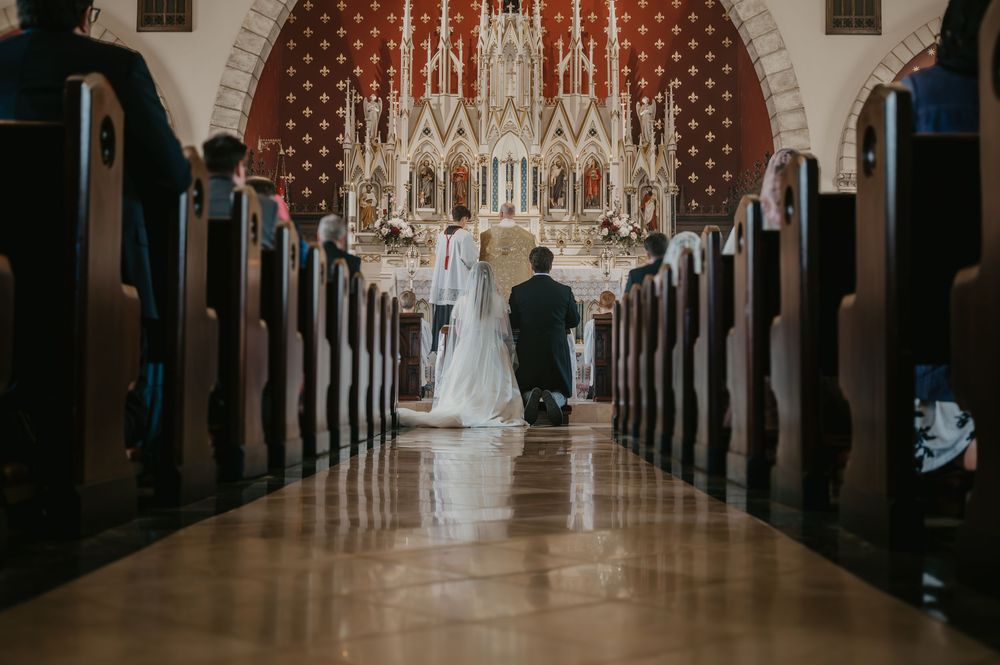 Bride and groom kneeling together at ornate Catholic church altar during traditional wedding ceremony.