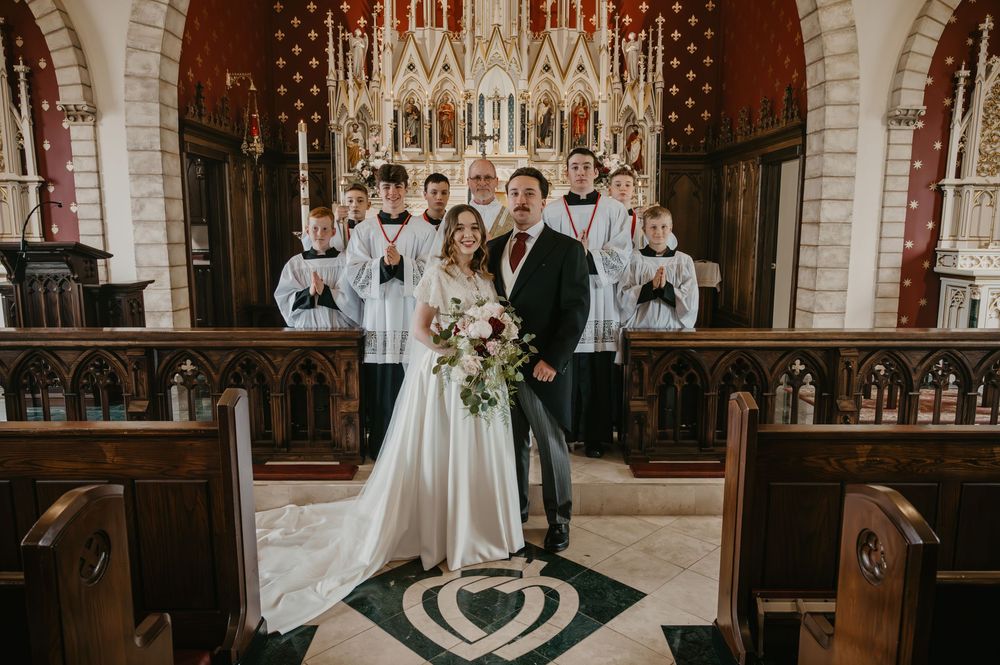 Newlyweds posing with altar servers inside stunning Gothic Catholic church after wedding ceremony.