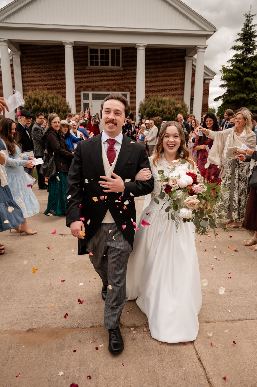 Joyful newlyweds exit church as guests shower them with colorful flower petals after wedding ceremony.