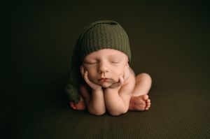 Close-up portrait shot of a sleeping baby wrapped in a brown knitted blanket against a dark background.