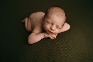 Sleeping newborn peacefully rests on olive green textured fabric in artistic portrait setting.