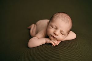 Peaceful sleeping newborn baby rests on textured olive green blanket with hands clasped under head.