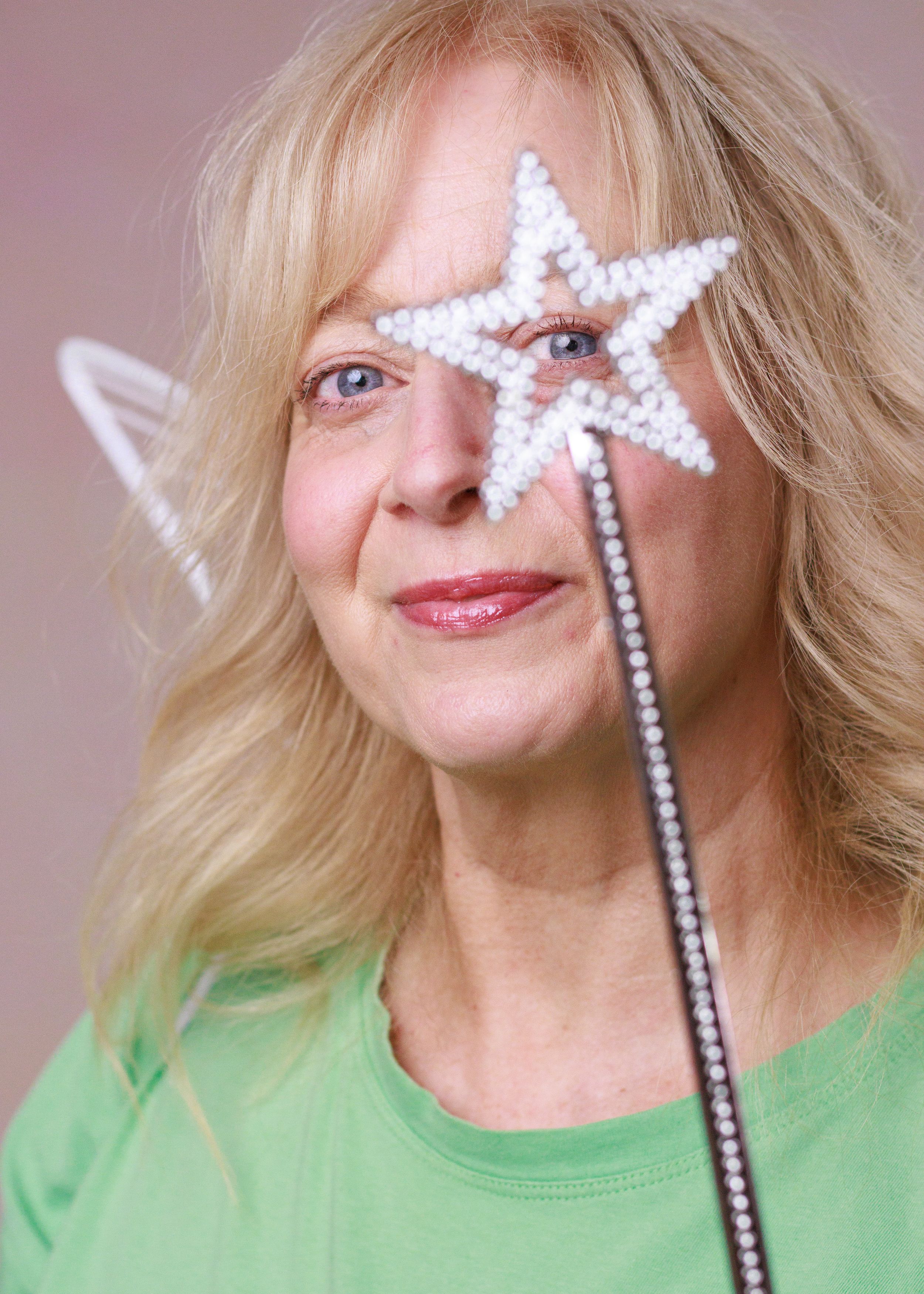 A bright pearl-encrusted magic wand in the shape of a star is held up to a smiling face against a soft pink background.