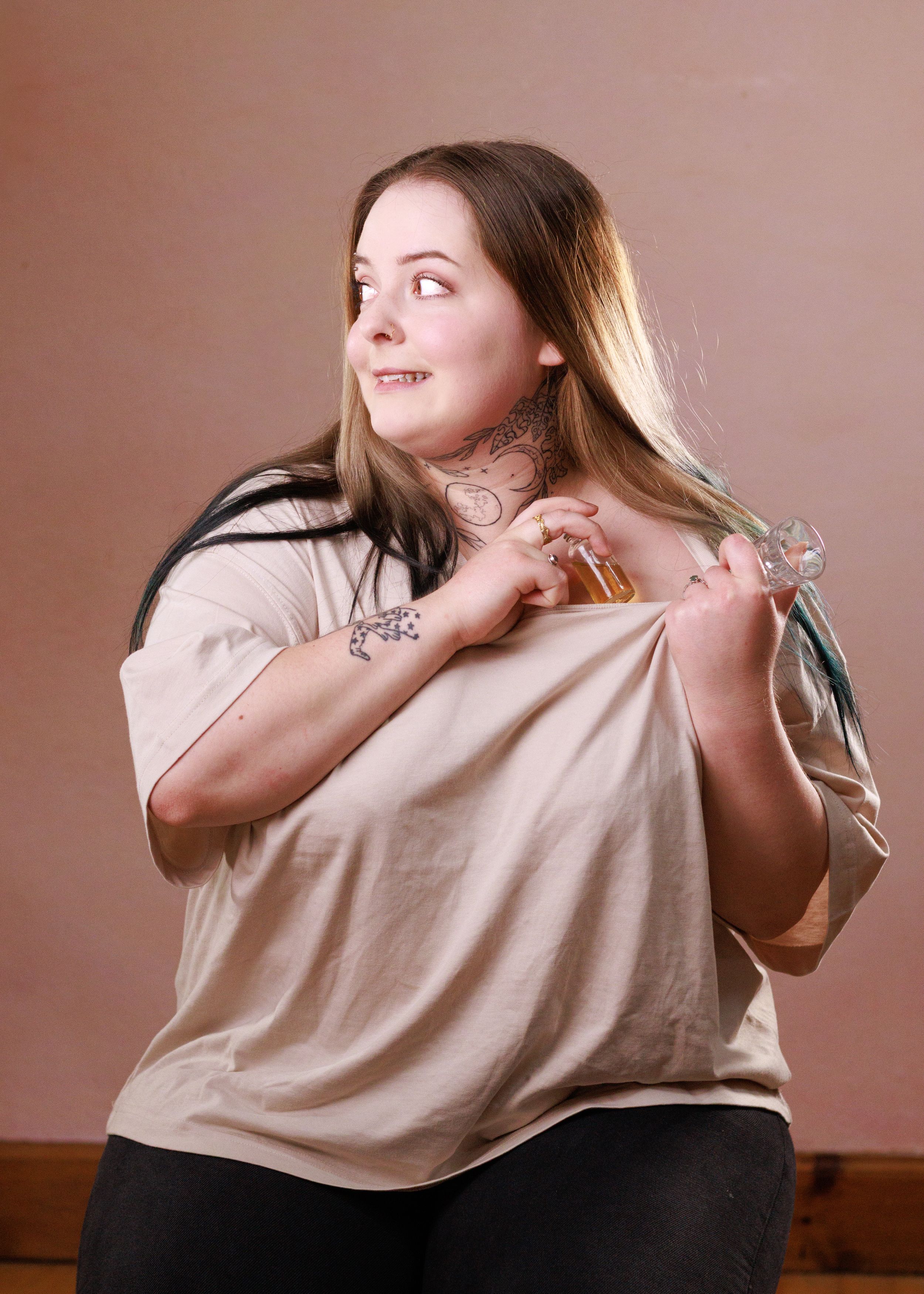 A person with long hair demonstrates how to put on a light colored t-shirt in a sequence of photos against a pink background.