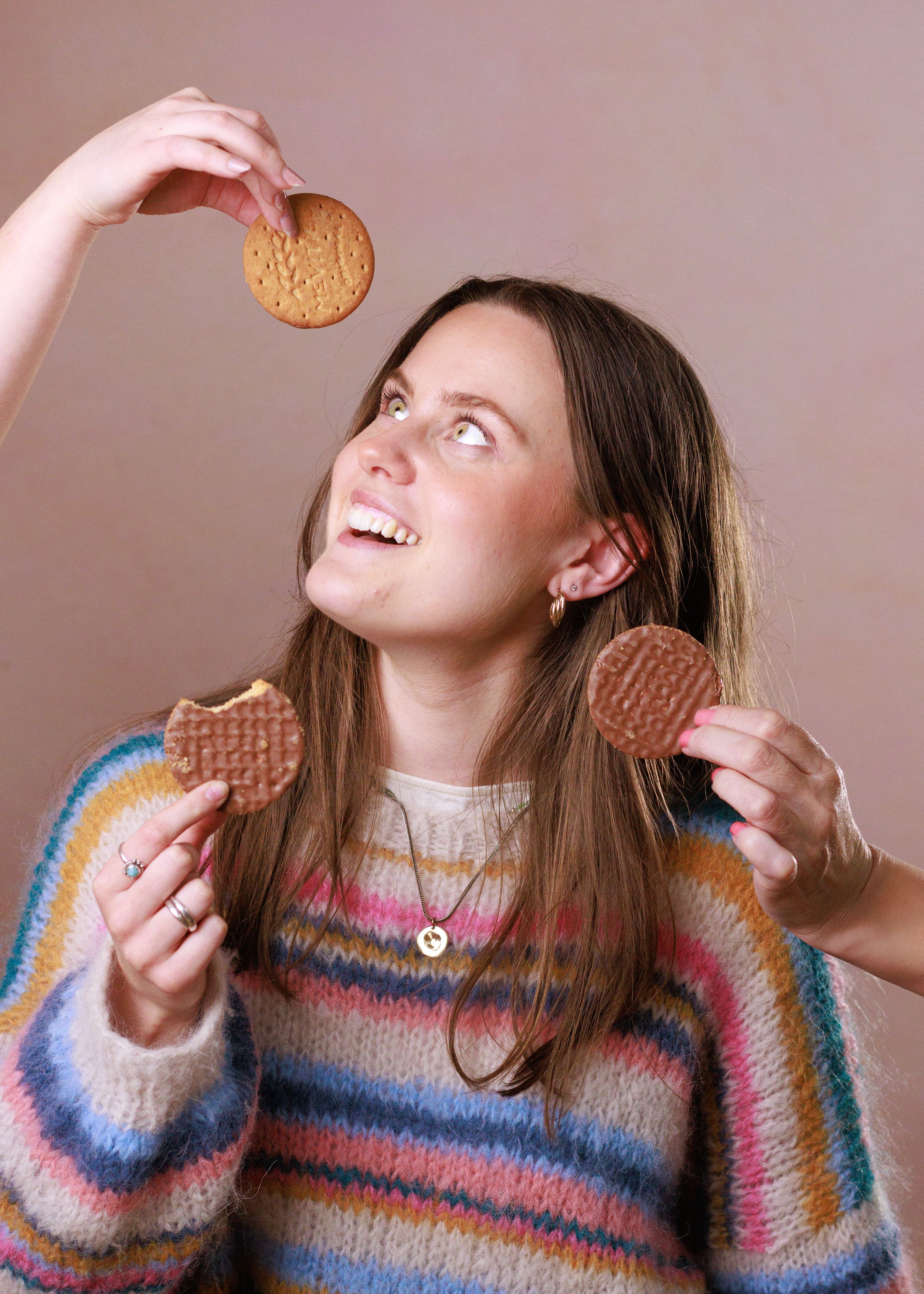 A person in a striped rainbow sweater takes a bite of a sandwich cookie while making playful expressions in a photo series.