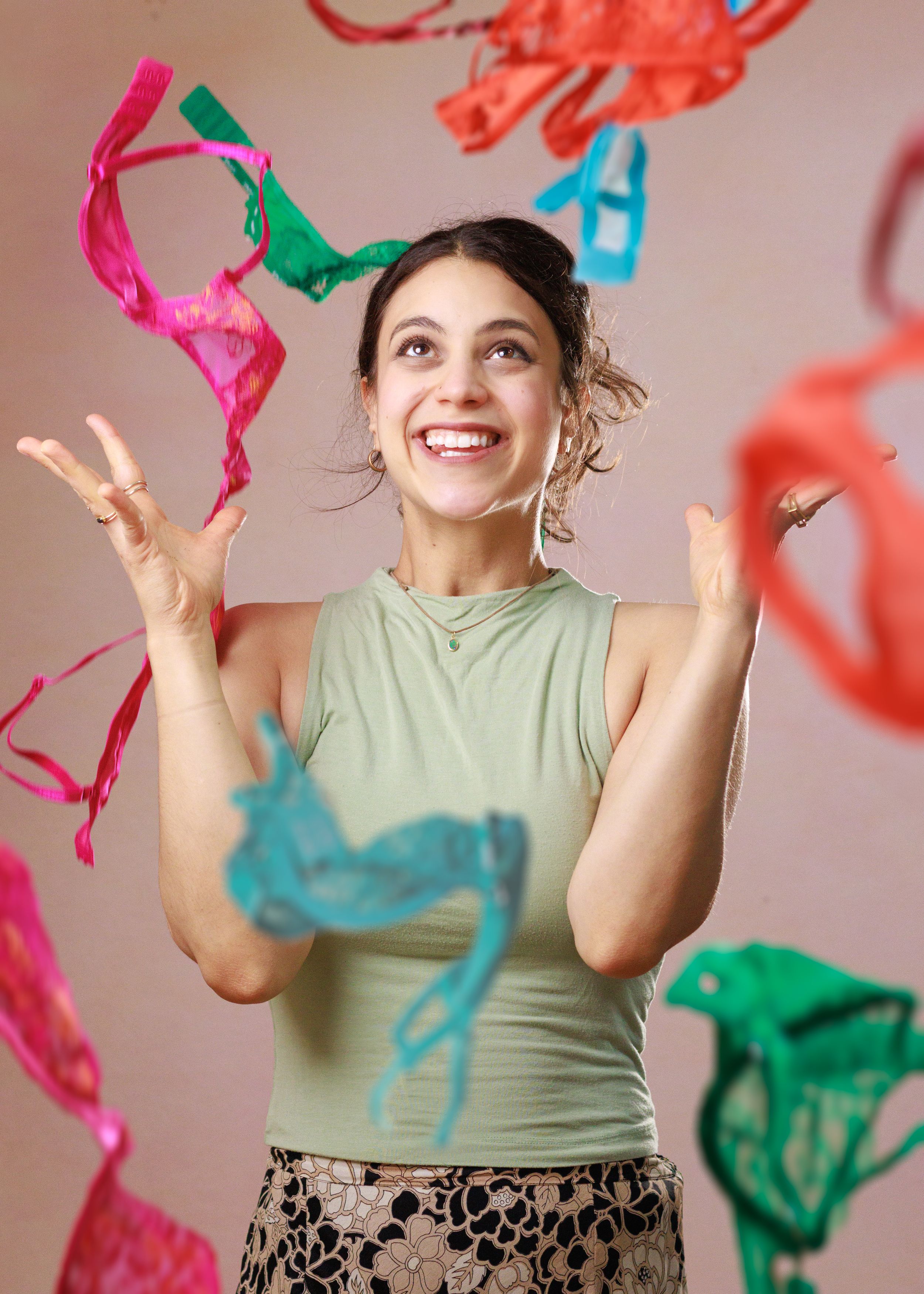 Joyful person in a sage green tank top tossing colorful tissue paper confetti against a light background.