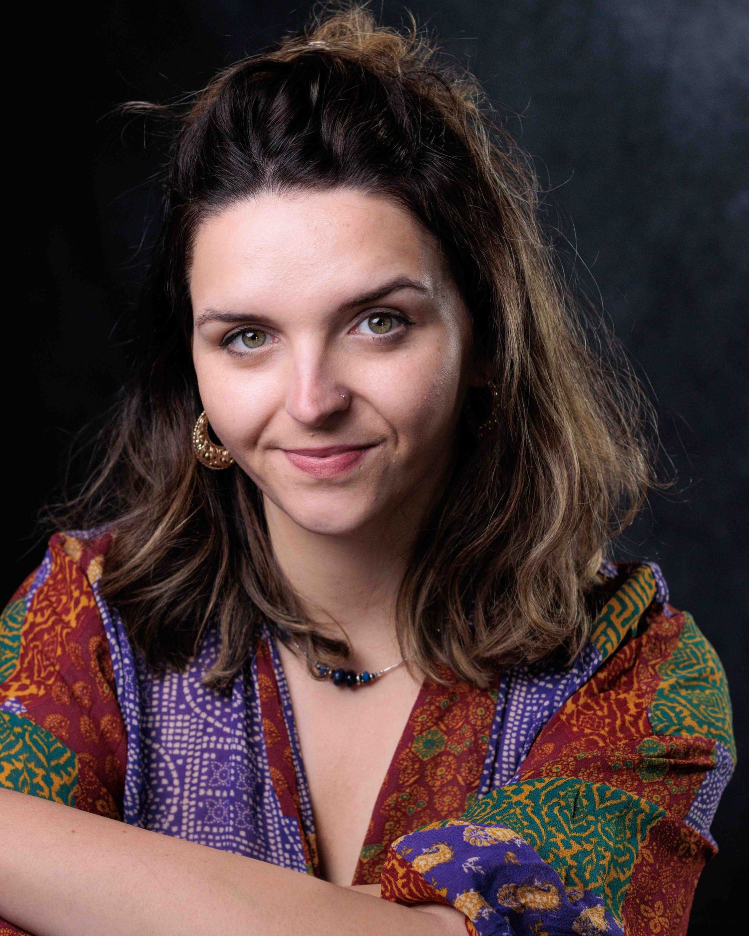 Portrait of a person with brown hair wearing a colorful patterned scarf in vibrant purple and red tones against dark background.