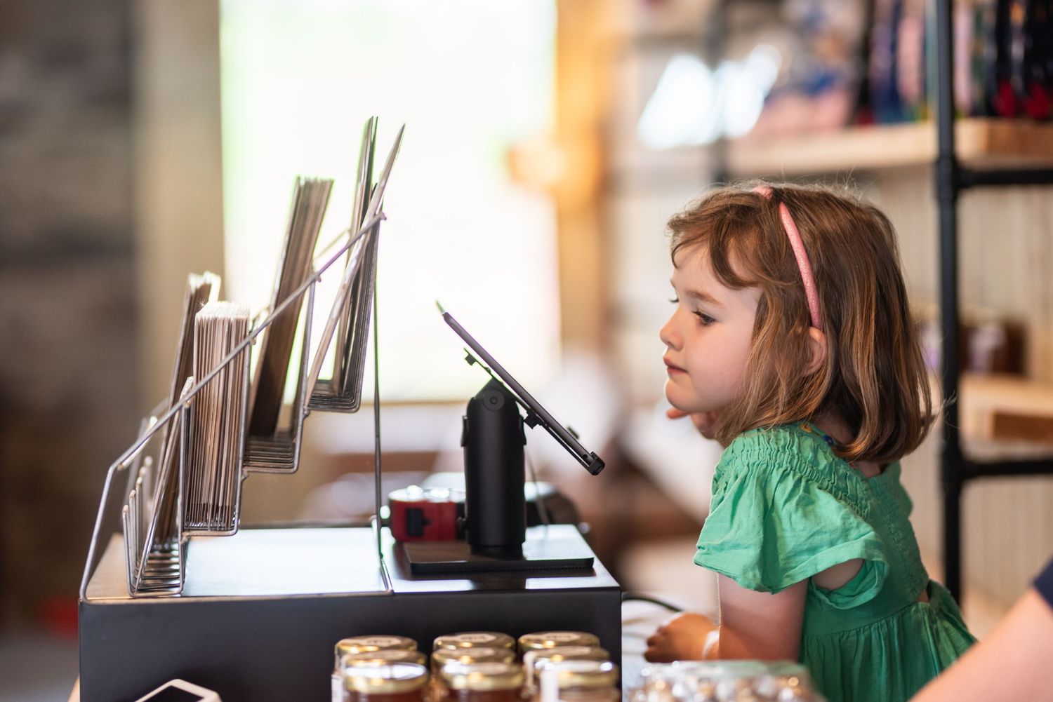 Young child in green dress using digital device at counter.