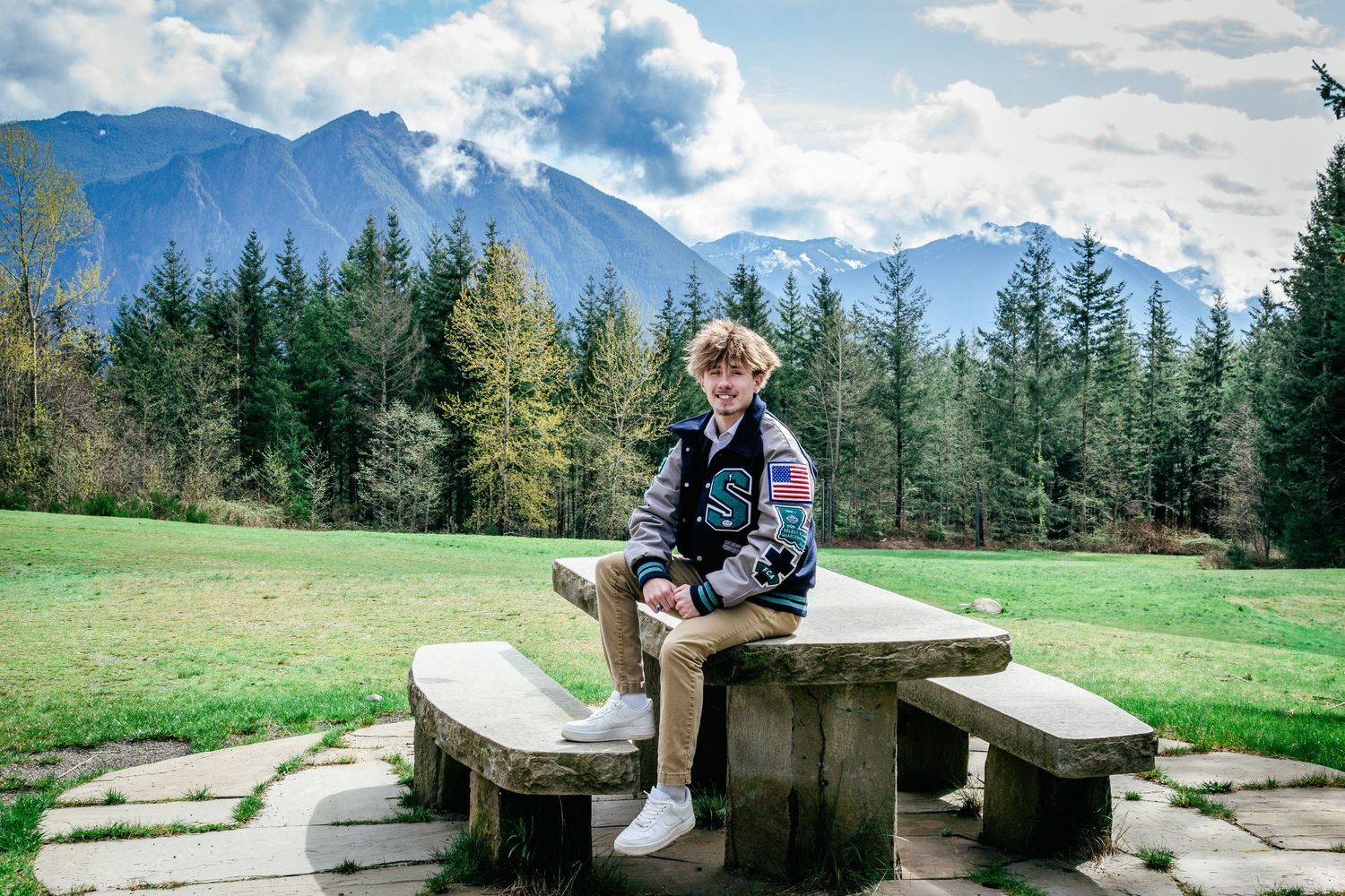 Senior portrait with mountains at Snoqualmie Point Park in Washington. A bold, scenic backdrop for a classic letterman jacket pose.