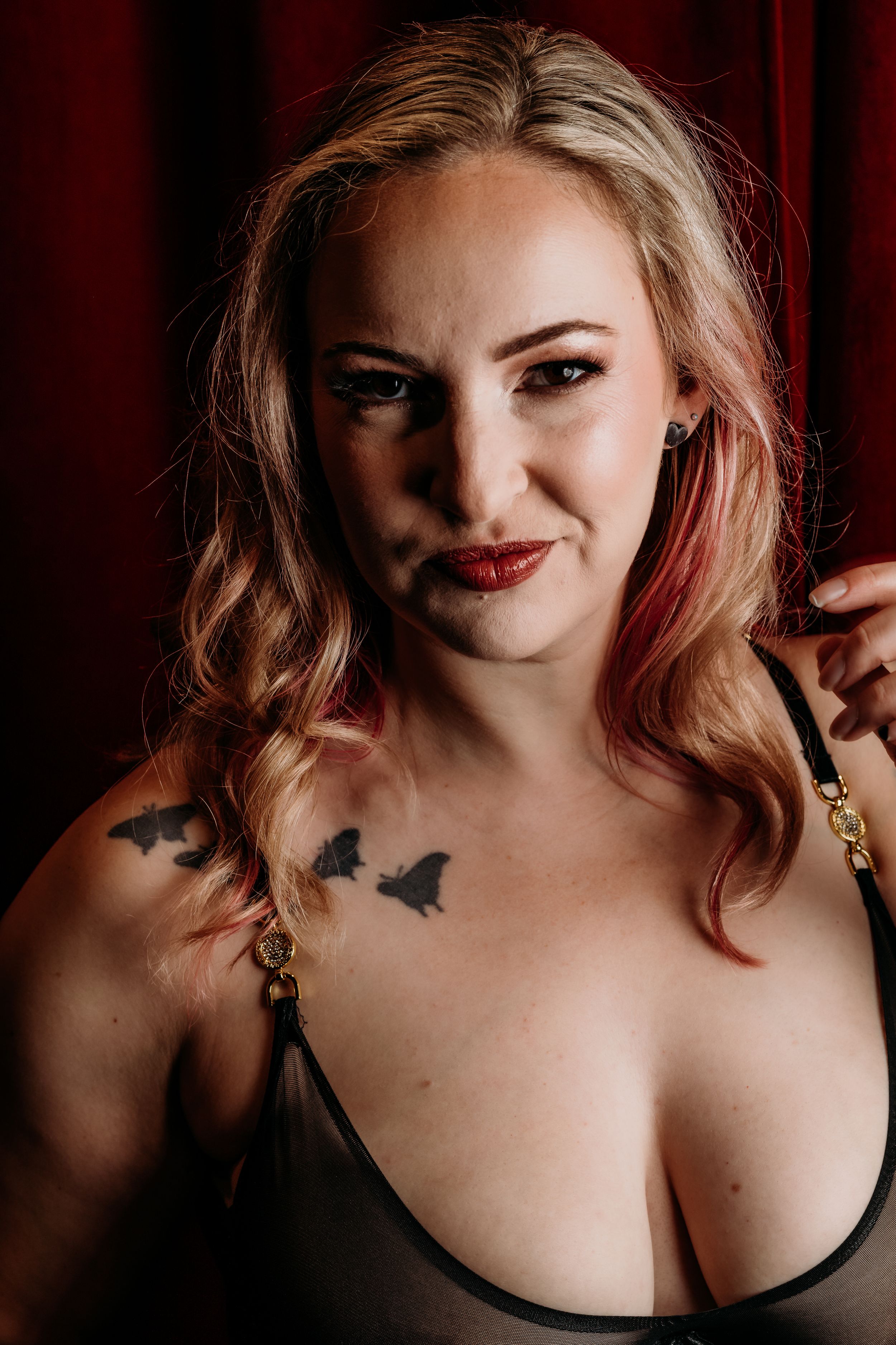 Portrait against red curtain background showcasing butterfly tattoo art and moody dramatic lighting.Grand Rapids Boudoir Photography
