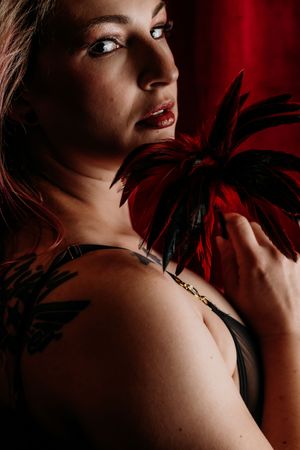 Artistic portrait with dramatic red lighting and black feather accents. Grand Rapids Boudoir Photography Mini Session Marathon