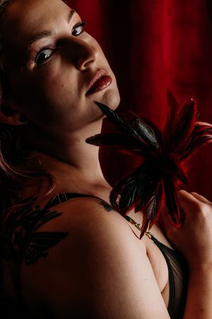 Dramatic noir-style portrait with red velvet curtain backdrop and black feather accessories. Grand Rapids Boudoir Photography