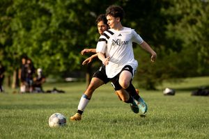 Soccer players compete for possession of the ball during a match on a sunny grass field.