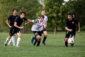 Soccer players in black and white uniforms compete for the ball during an outdoor match on a grass field.