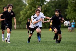 Soccer players in black and white uniforms dash across a green grass field during a competitive match.