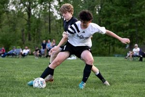 Two youth soccer players battling for possession of the ball on a grassy field during a competitive match.