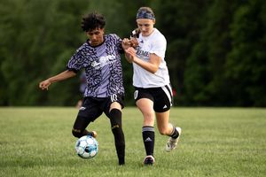 Two soccer players slide across grass field battling for possession of the ball during competitive match.