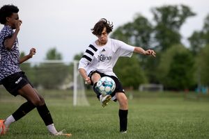 Soccer players compete for ball control during outdoor match on grass field.