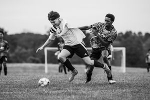 Two soccer players battle for possession of the ball during an intense match on a grass field.