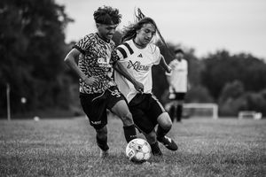Two soccer players compete for control of the ball during an intense black and white match on a grass field.
