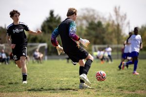 Soccer player in colorful tie-dye jersey kicking ball on grass field during outdoor match.