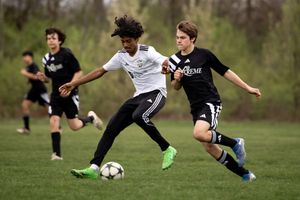 Youth soccer players compete for possession of the ball during an intense match on a grass field.