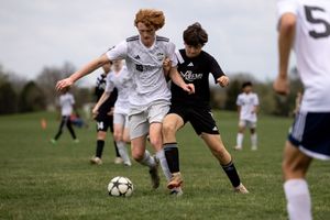 Soccer players battle for possession of the ball during competitive match on grass field.