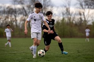 Two youth soccer players compete for the ball during a match, with one in white and one in black uniforms.