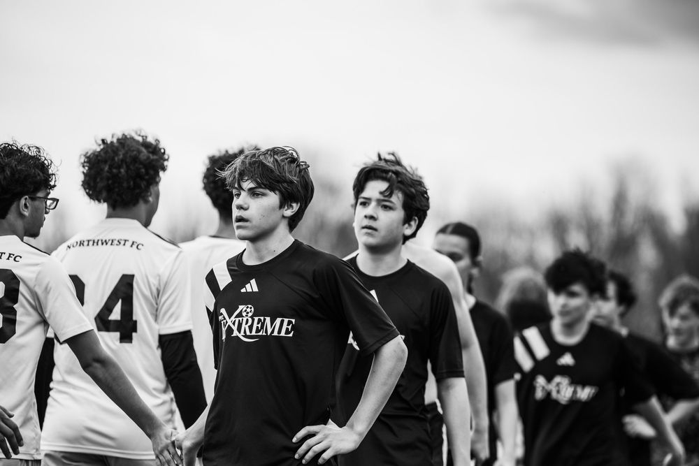 Black and white photo of rugby players during a match pause wearing contrasting uniforms and standing on the field.