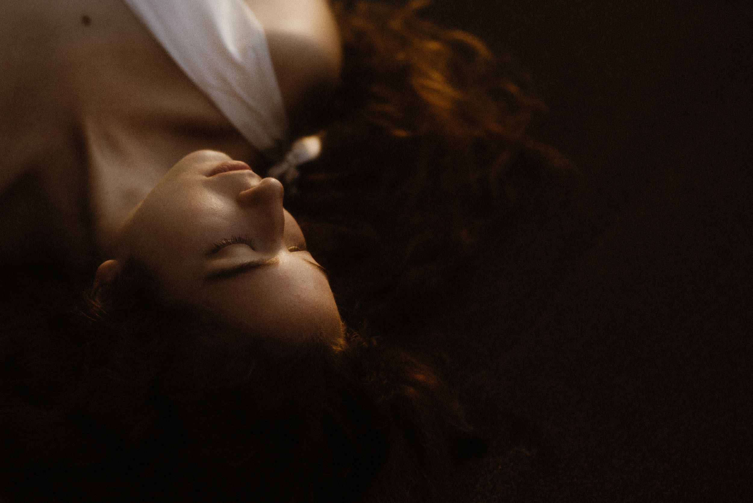 Close-up portrait in warm natural lighting captures peaceful expression in a dark, moody atmosphere at Los Gigantes, Tenerife.