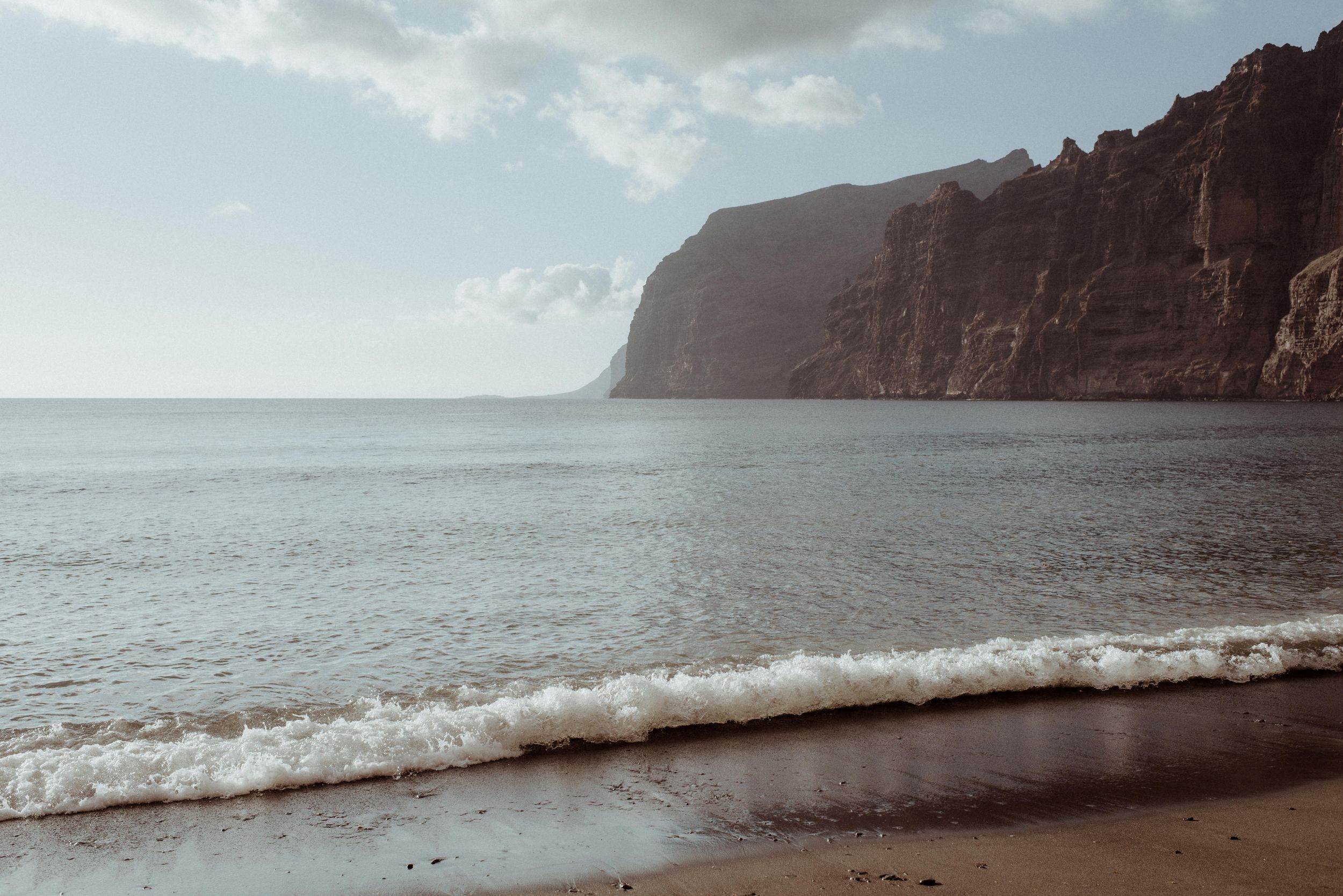 A panoramic series of ocean waves crashing on a rocky beach with dramatic cliffs in the misty background of Los Gigantes.