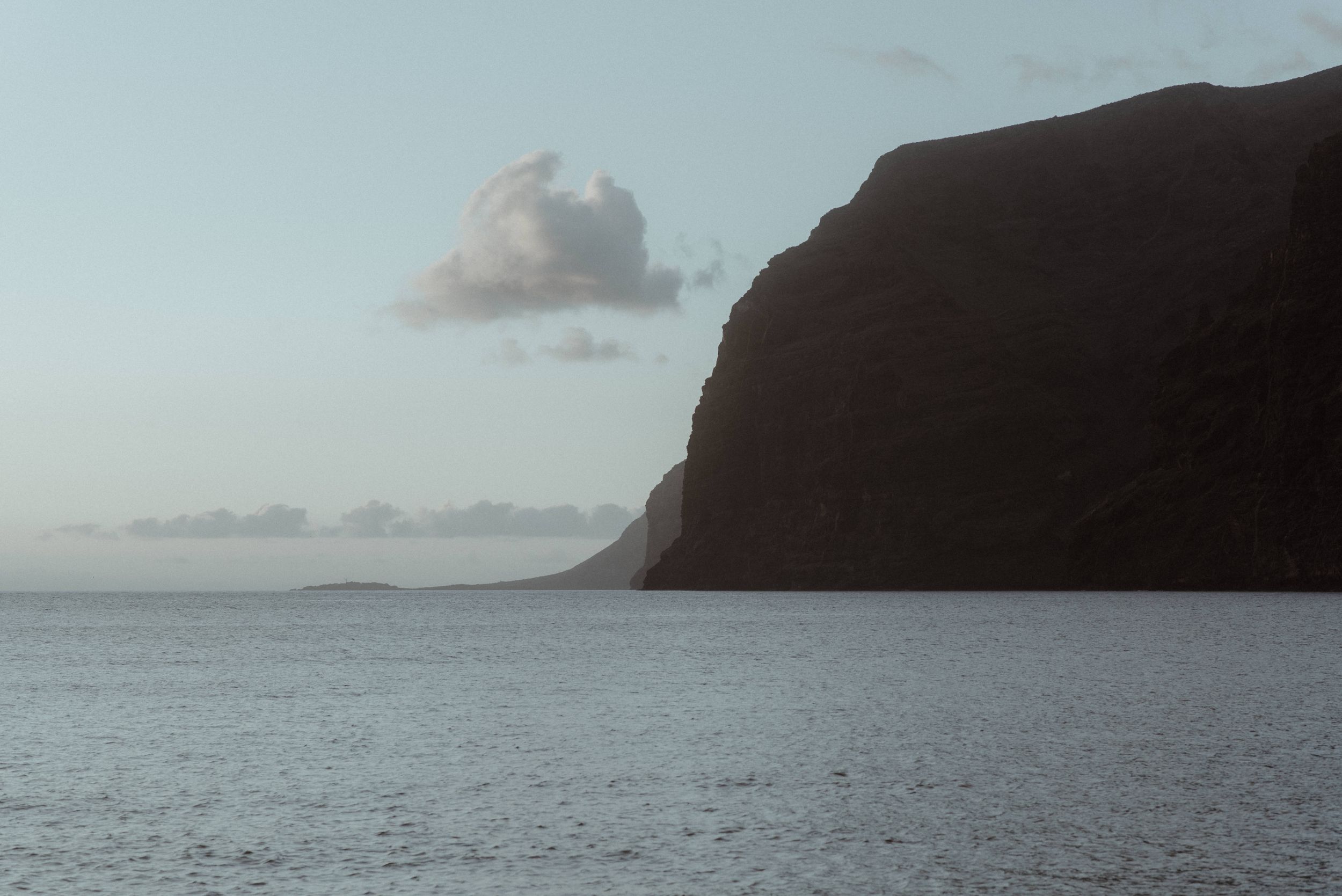 Misty coastal seascape with dramatic cliff silhouette against a pale sky over calm ocean waters of Los Gigantes.