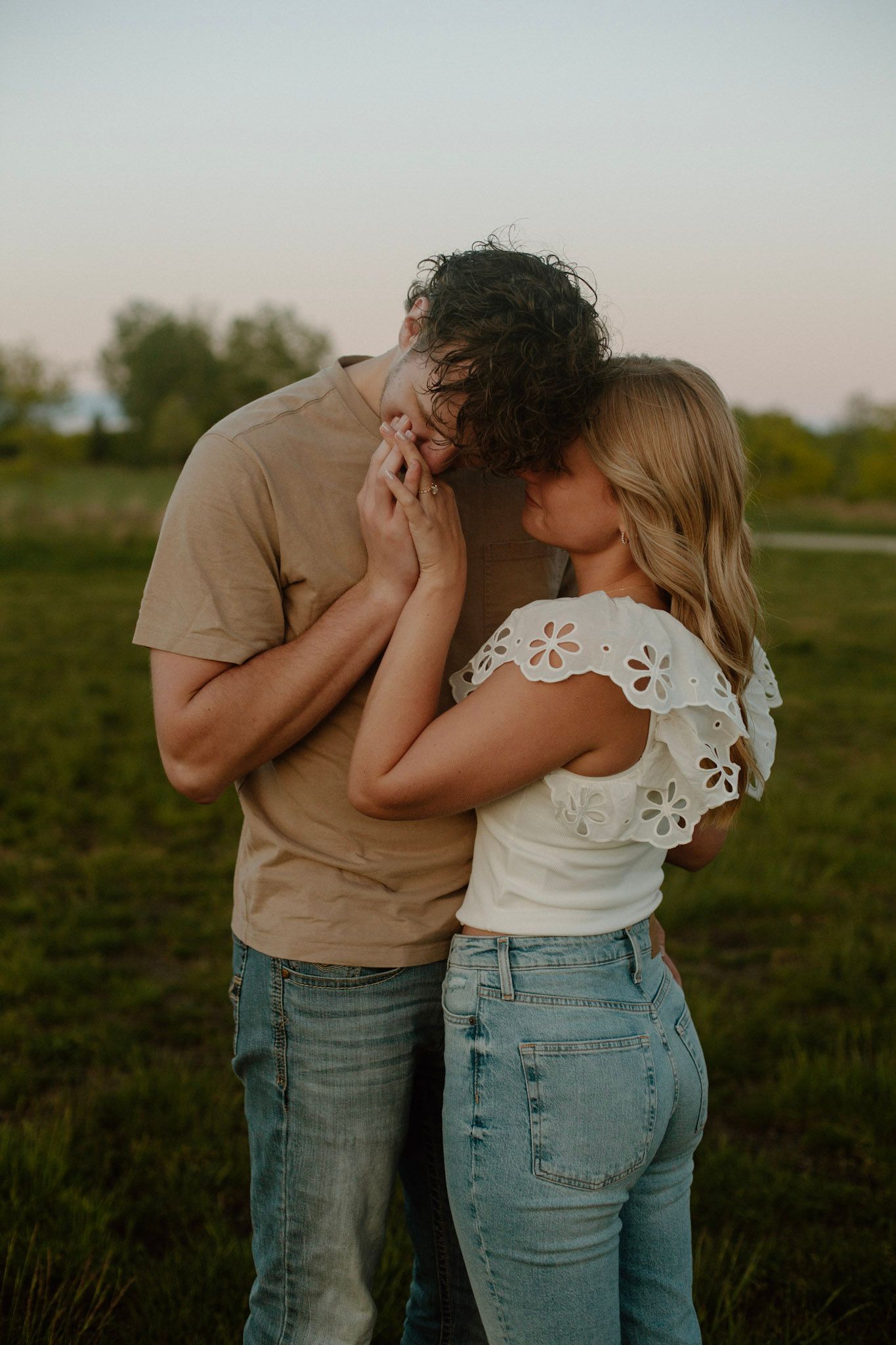 Couple embracing during their engagement session at Millennium Park in Grand Rapids MI and he is kissing her hand.