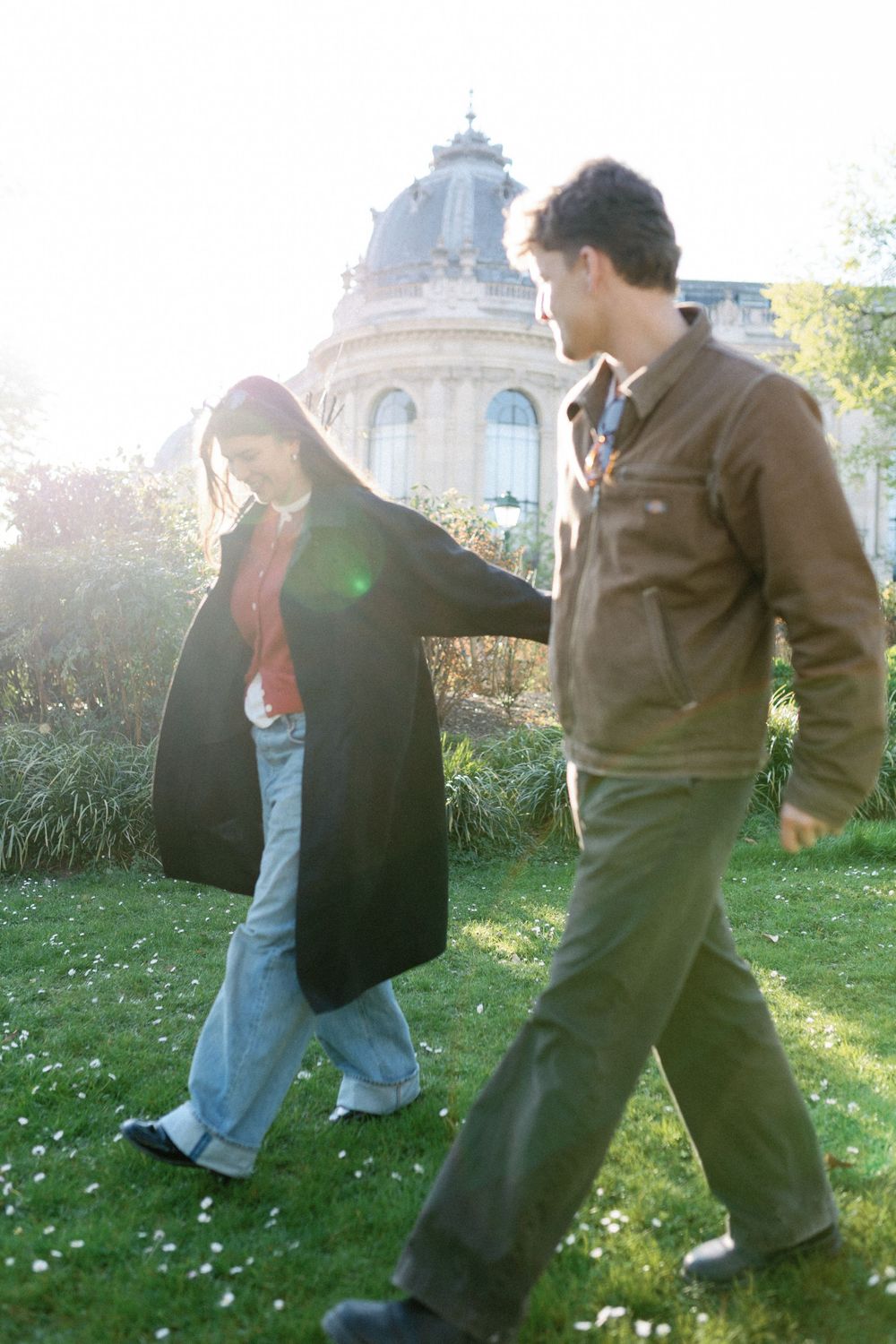 Two people practicing martial arts moves outside on a grassy lawn near ornate architecture buildings.