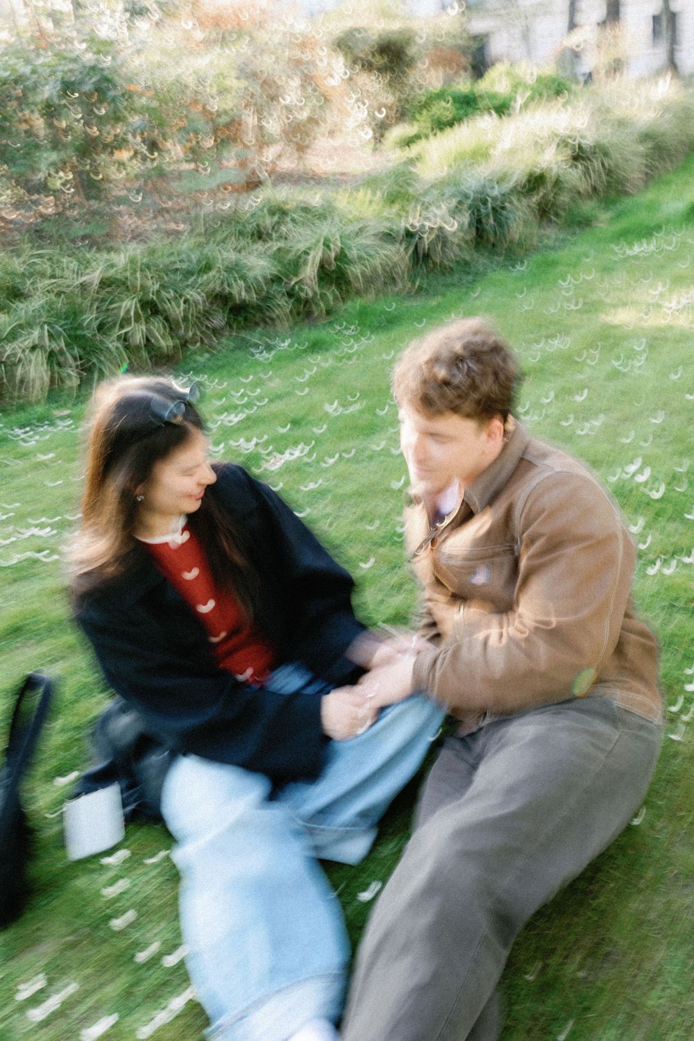 Two young people sitting together on a grassy slope in casual attire with a motion-blurred quality to the photo.