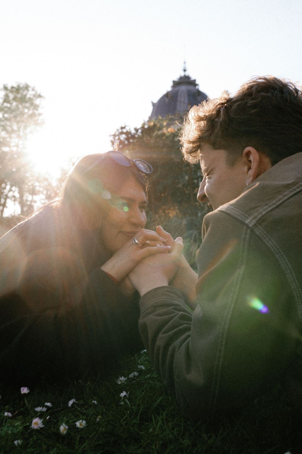 A tender romantic moment between a couple bathed in warm sunlight with a church spire visible in the background.