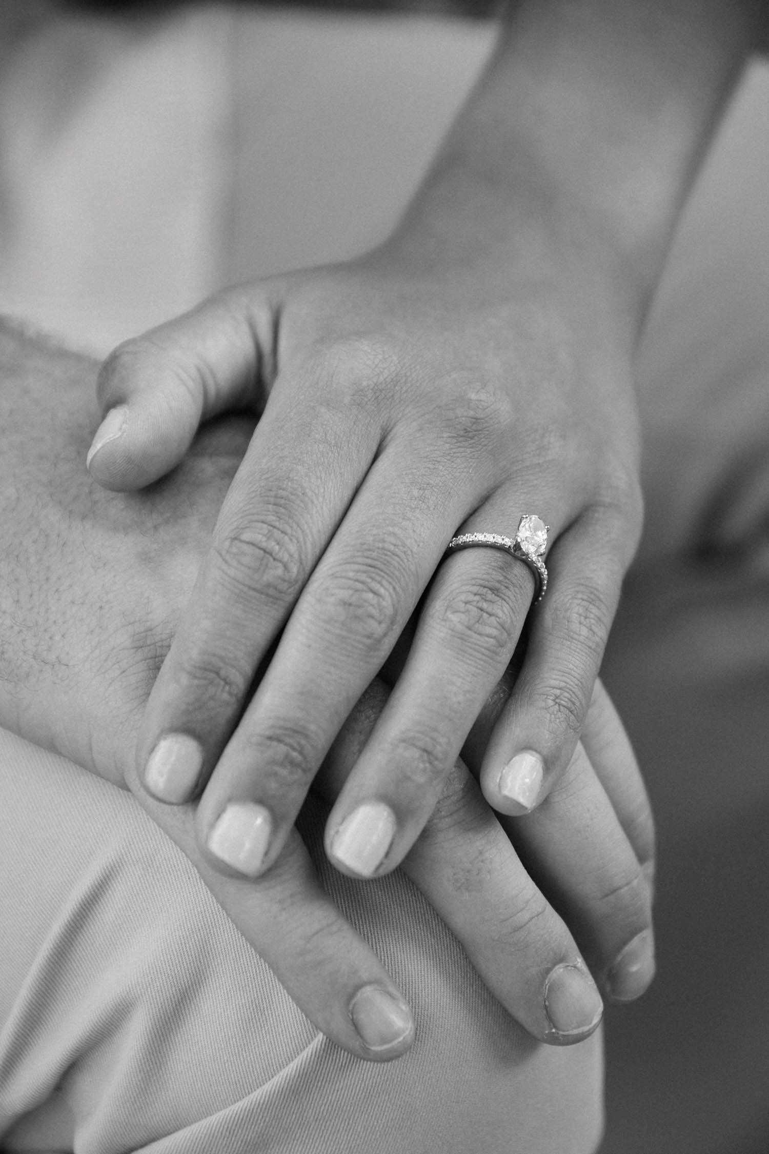 Close-up of hands with engagement ring in black and white.