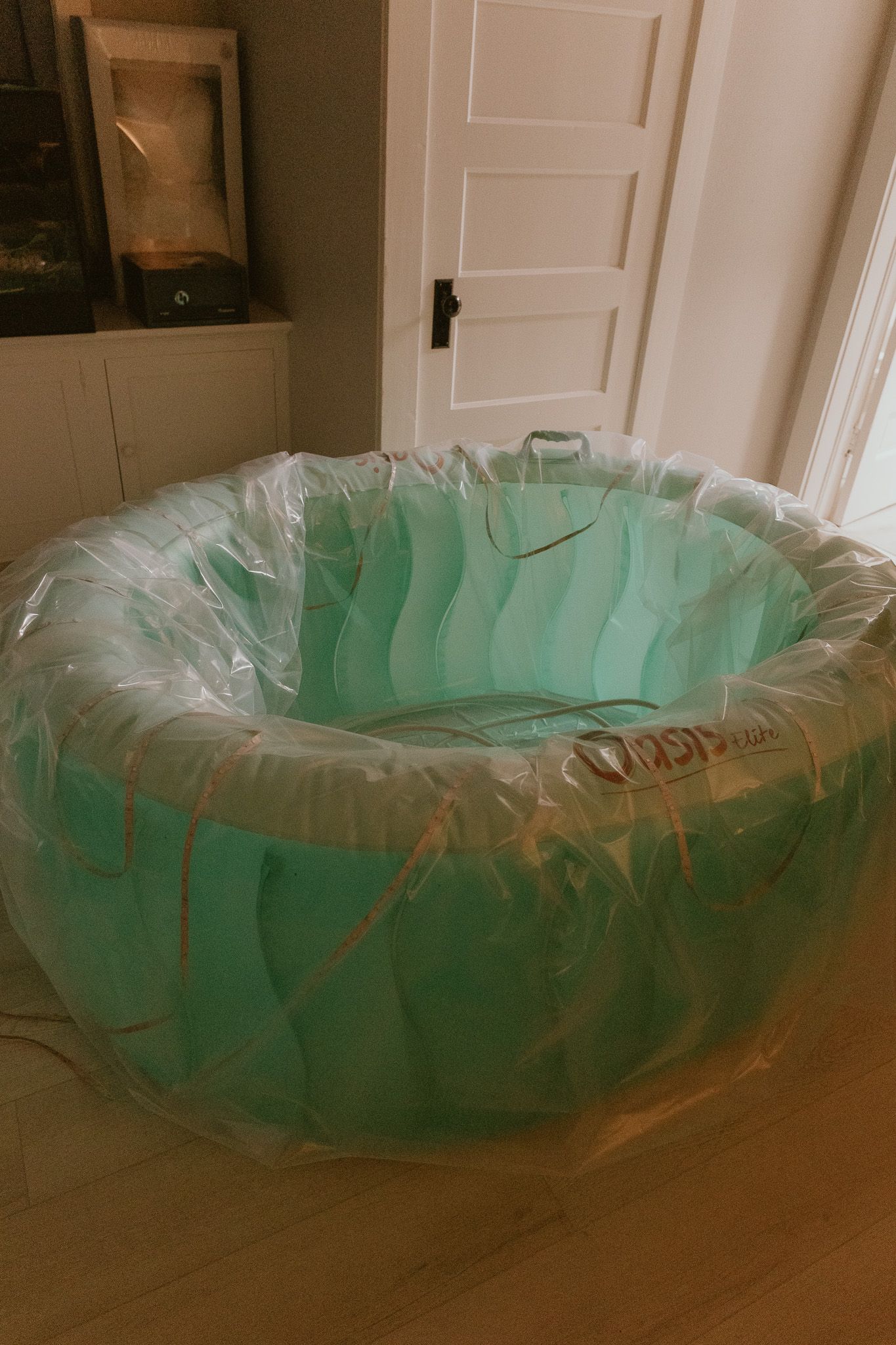 An inflatable teal-colored birth pool with protective liner sits empty on hardwood flooring near a white door.